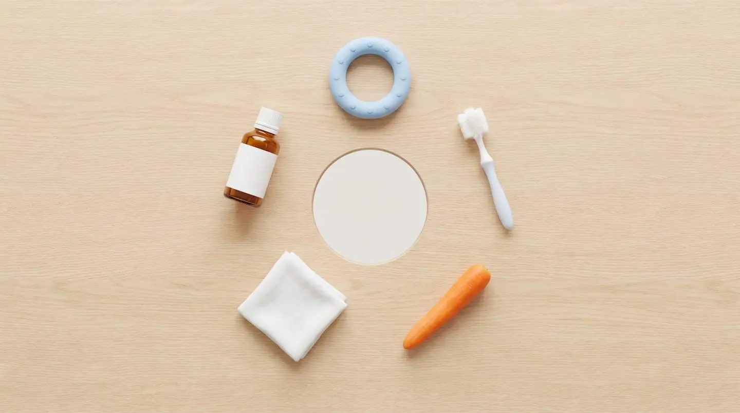 Cinq objets pour soulager la dentition disposés en cercle sur une table en bois : anneau de dentition, brosse, carotte, compresse et flacon